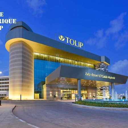 Tolip Resort El Galala Majestic Ain Sukhna Eksteriør bilde The photo shows a modern hotel building named "Tolip Resort & Spa," featuring a sleek architectural design with large glass windows. The hotel is illuminated against a twilight sky, showcasing its prominent signage. In the foreground, there is a well