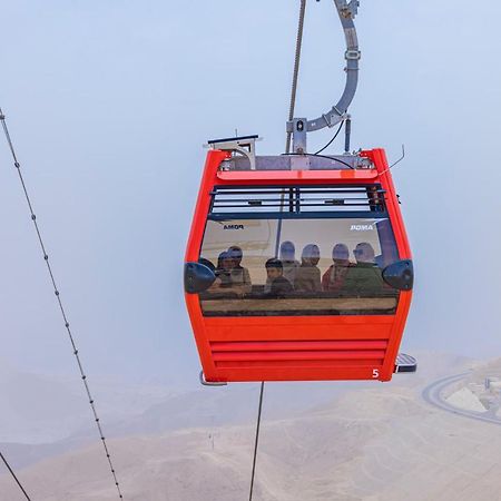 Tolip Resort El Galala Majestic Ain Sukhna Eksteriør bilde The photo shows a red gondola lift suspended in the air, traveling along cables. Inside the gondola, a group of people can be seen. The background features a hazy landscape, possibly mountains or hills, indicating an elevated area. The scene conveys 