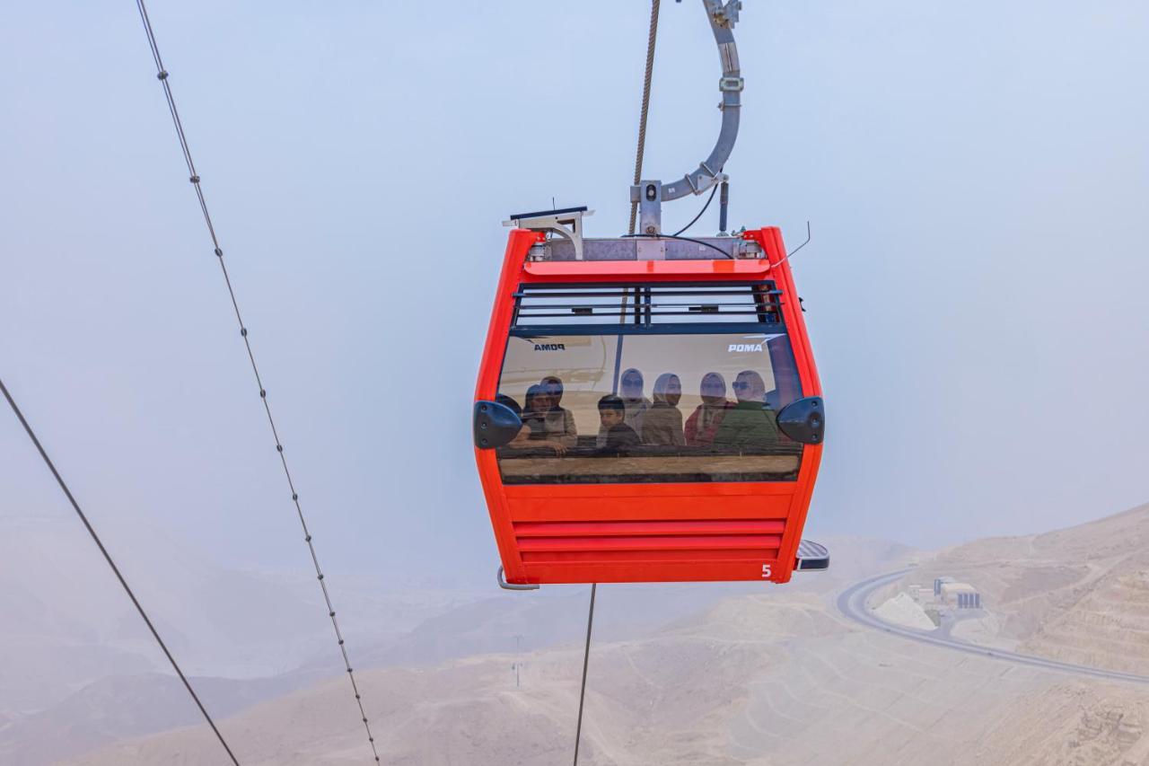 Tolip Resort El Galala Majestic Ain Sukhna Eksteriør bilde The photo shows a red gondola lift suspended in the air, traveling along cables. Inside the gondola, a group of people can be seen. The background features a hazy landscape, possibly mountains or hills, indicating an elevated area. The scene conveys 