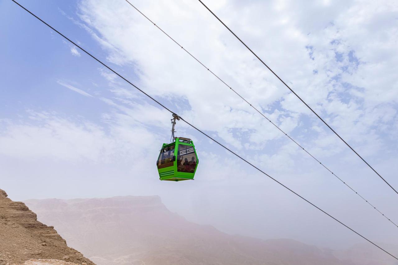 Tolip Resort El Galala Majestic Ain Sukhna Eksteriør bilde The photo shows a green cable car suspended in the air, traveling along overhead cables. The backdrop features a hazy landscape, likely mountainous or elevated terrain, with a cloudy sky. The scene suggests a scenic transportation method, possibly us