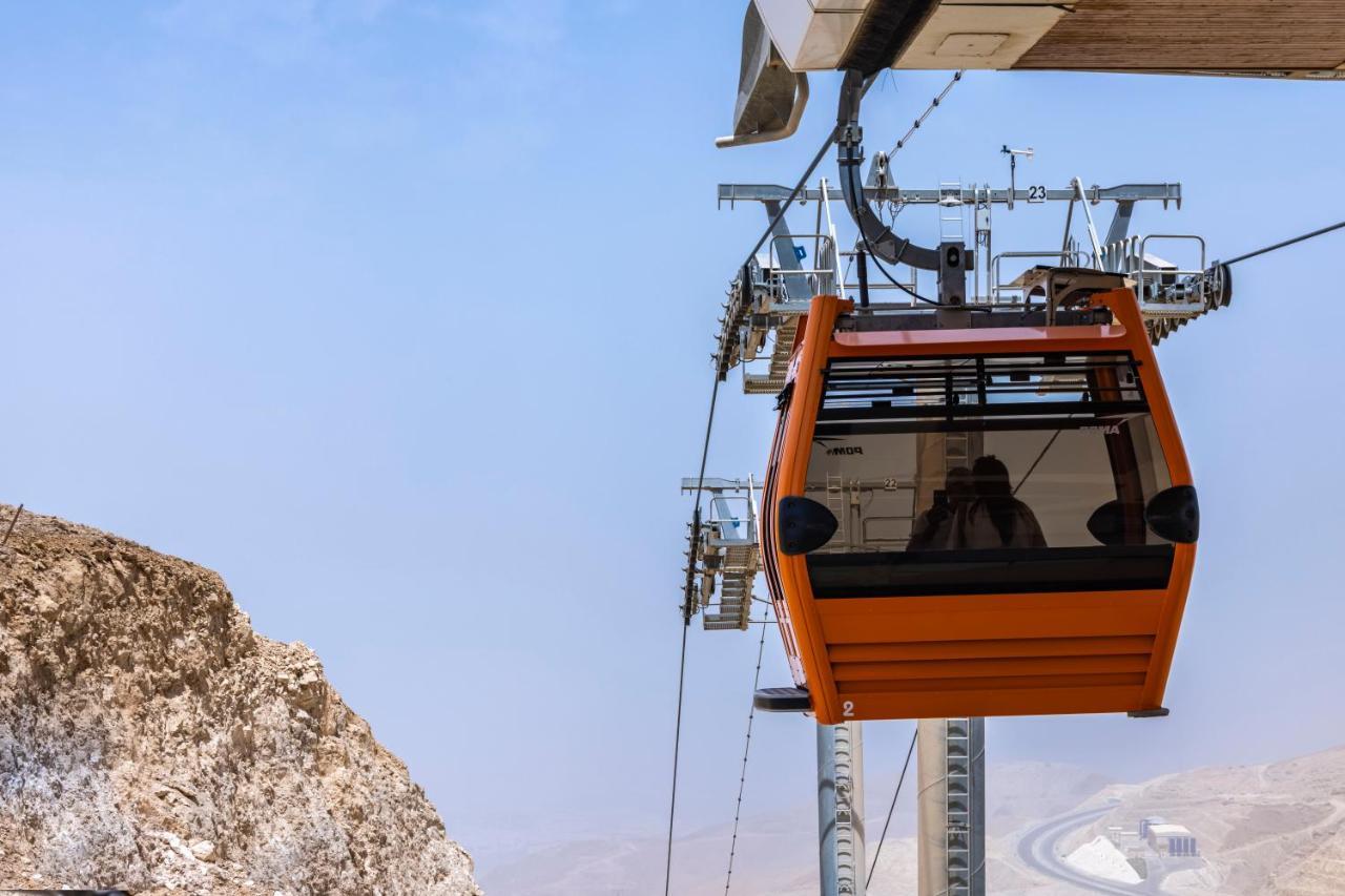 Tolip Resort El Galala Majestic Ain Sukhna Eksteriør bilde The photo shows an orange gondola or cable car hanging on a cable system. The gondola appears to be suspended in the air above a rocky landscape, with a clear sky in the background. There are supporting cables and structures visible, indicating that 