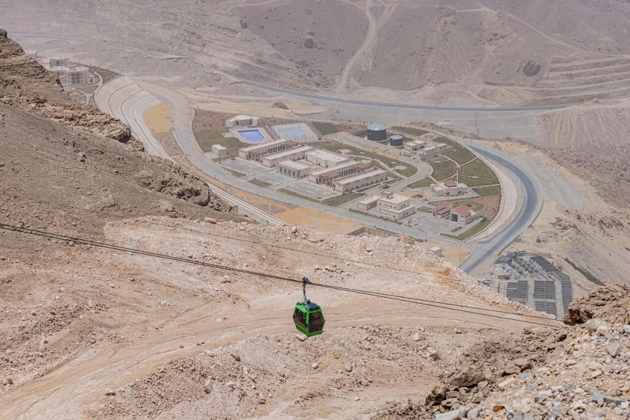 Tolip Resort El Galala Majestic Ain Sukhna Eksteriør bilde The photo shows a mountainous landscape with a steep, dry terrain. In the foreground, there is a green cable car or gondola traveling along a cable. Below, a complex of buildings and roads can be seen, likely part of a resort or recreational area. Th