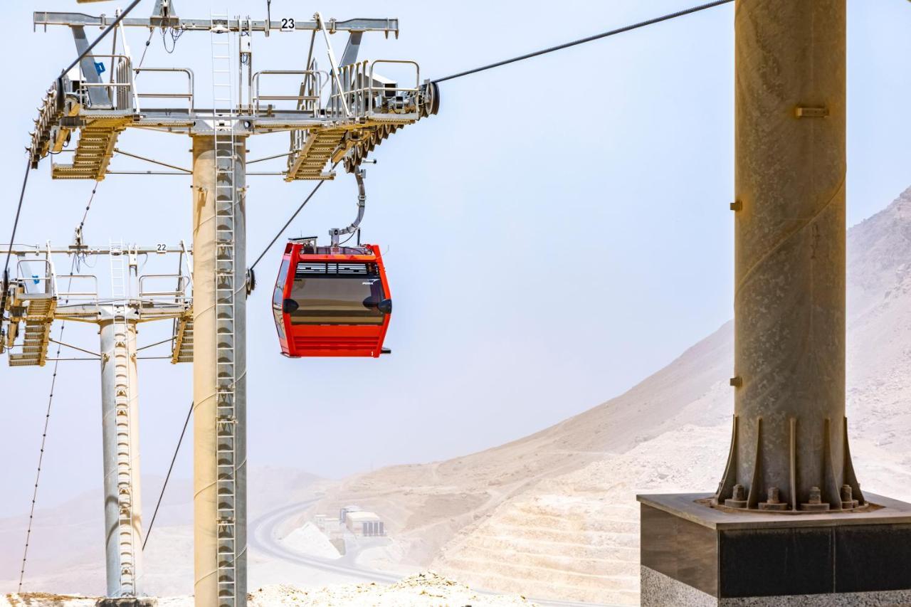 Tolip Resort El Galala Majestic Ain Sukhna Eksteriør bilde The photo shows a cable car system with a single red gondola suspended mid-air. It appears to be part of a larger cable car infrastructure, with metal pylons supporting the cables above. The background features a hazy landscape, likely characterized 