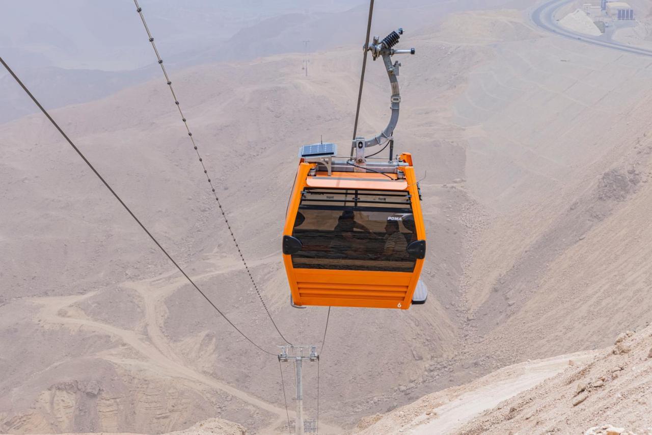 Tolip Resort El Galala Majestic Ain Sukhna Eksteriør bilde The photo shows an orange cable car suspended in the air, traveling along a set of cables. It appears to be located in a mountainous or hilly area, with rugged terrain and dry, rocky landscapes visible below. The background features slopes that seem 