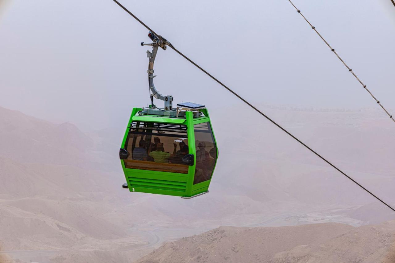 Tolip Resort El Galala Majestic Ain Sukhna Eksteriør bilde The photo shows a green cable car suspended in the air, moving along a wire. The cable car appears to be traversing a mountainous landscape, which looks rocky and arid. The surrounding environment is somewhat foggy or hazy, suggesting limited visibil