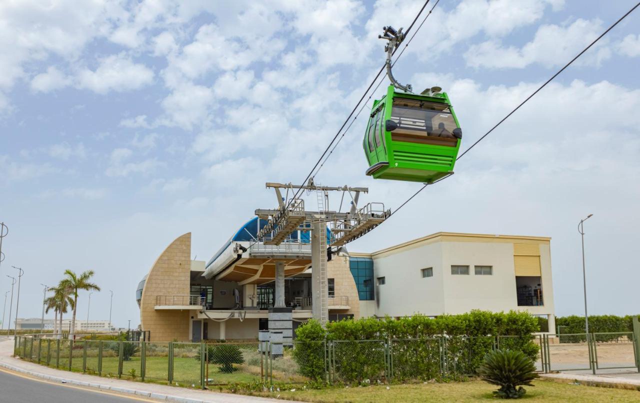 Tolip Resort El Galala Majestic Ain Sukhna Eksteriør bilde The photo shows a cable car or gondola system in operation, featuring a green-colored gondola. It is suspended from cables and moving towards a station, which appears to be a modern building with a unique architectural design. The station has large w