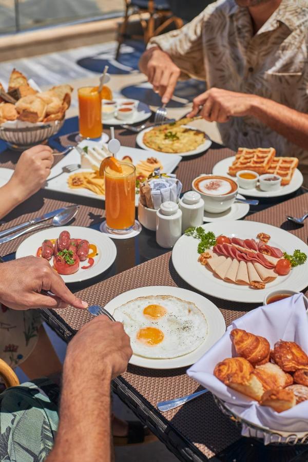 Tolip Resort El Galala Majestic Ain Sukhna Eksteriør bilde The photo features a spread of breakfast dishes on a table. There are two sunny-side-up eggs on one plate, surrounded by various food items, including slices of ham, sausages, and fresh tomatoes. Another plate holds a serving of waffles. A bowl with 