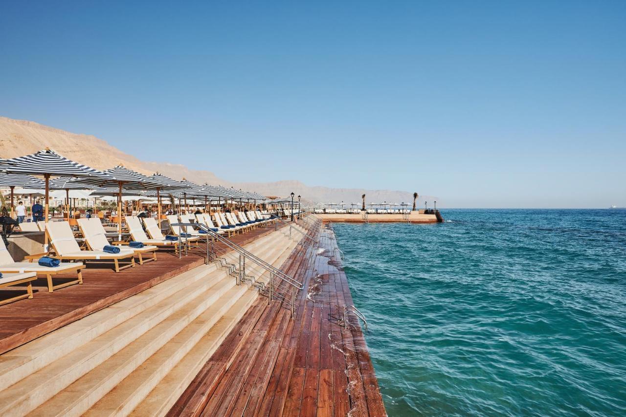 Tolip Resort El Galala Majestic Ain Sukhna Eksteriør bilde The photo shows a seaside area featuring a wooden deck that extends into the water. On the left side, there are several lounge chairs arranged neatly under shade structures, suggesting a relaxing atmosphere. The ocean is visible in the foreground, wi