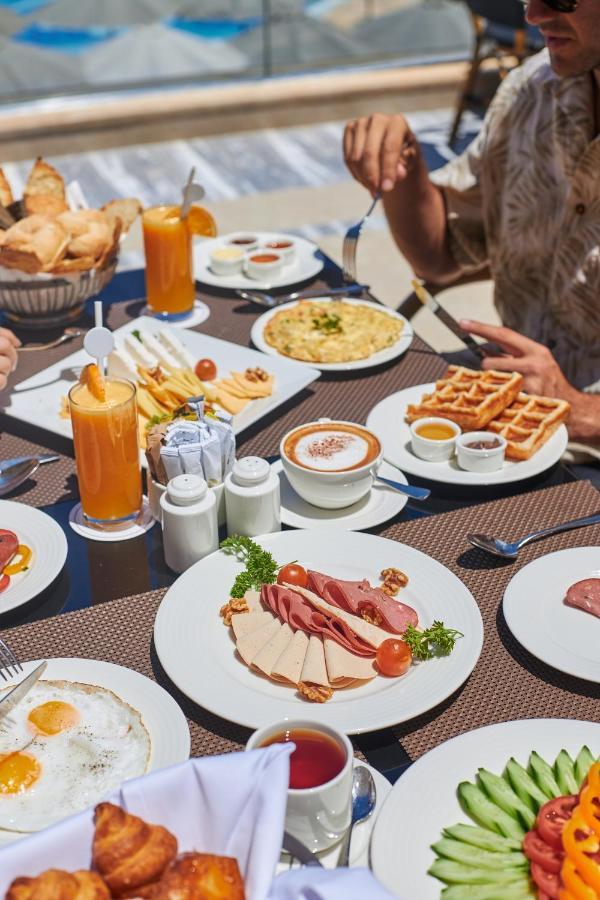 Tolip Resort El Galala Majestic Ain Sukhna Eksteriør bilde The photo shows a breakfast spread laid out on a table. There are several plates with a variety of food items, including:

1. **Sliced Cold Cuts**: A plate featuring various cold meats, accompanied by garnishes like cherry tomatoes and lettuce.
2. **