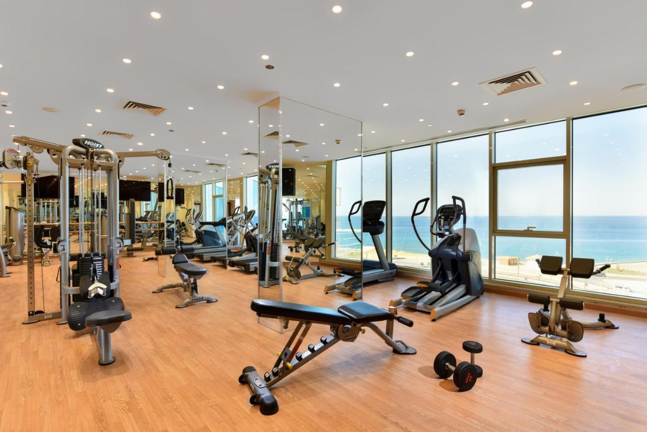 Tolip Resort El Galala Majestic Ain Sukhna Eksteriør bilde The photo shows a modern gym interior with a variety of fitness equipment. There are cardio machines like treadmills and ellipticals, along with strength training equipment such as free weights and benches. The gym features large windows that offer a